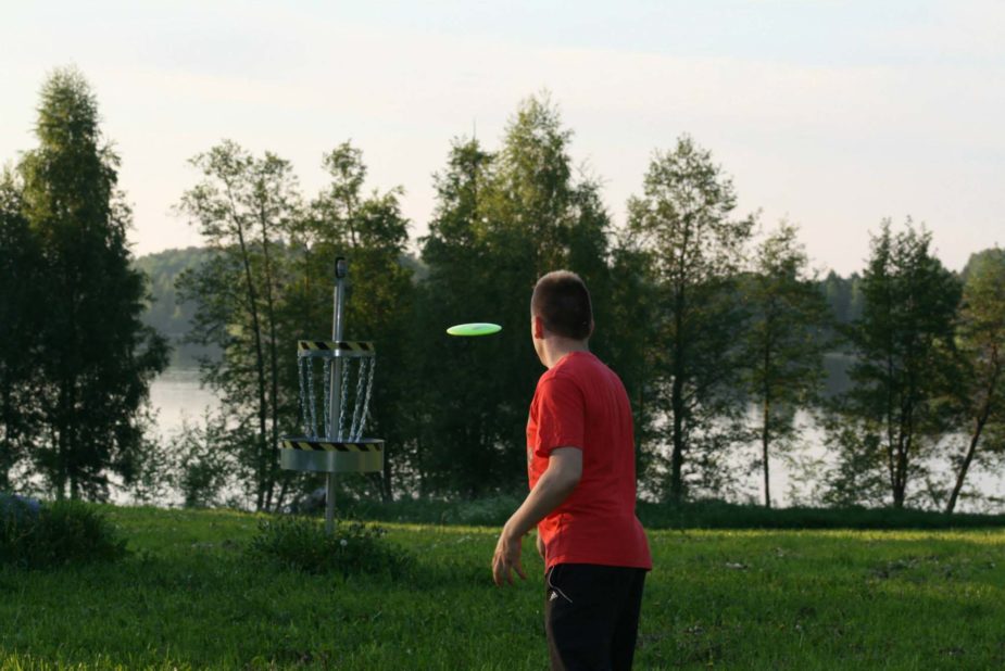 Frisbeegolfia kesäillassa Kanta-Hämeessä, kiekko matkalla kohti koria.