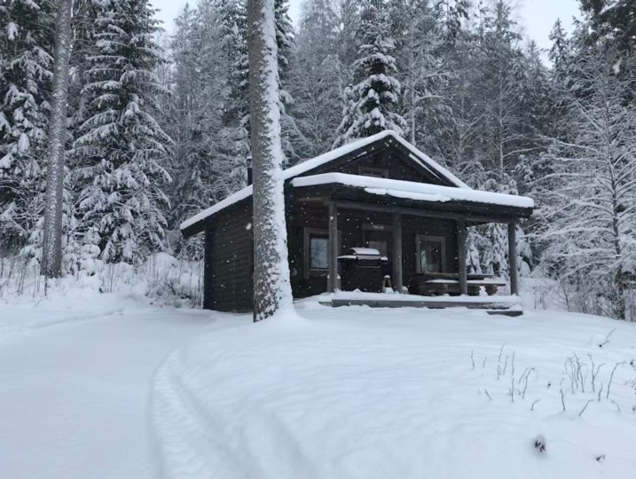 Aino-torppa talvimaisemissa lumihiutaleiden leijuessa.