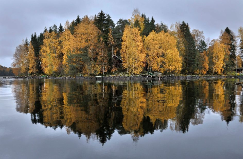 Ruskan värittämät puut heijastuen järven pintaan, puiden takaa pilkottaa Kärkimökki.