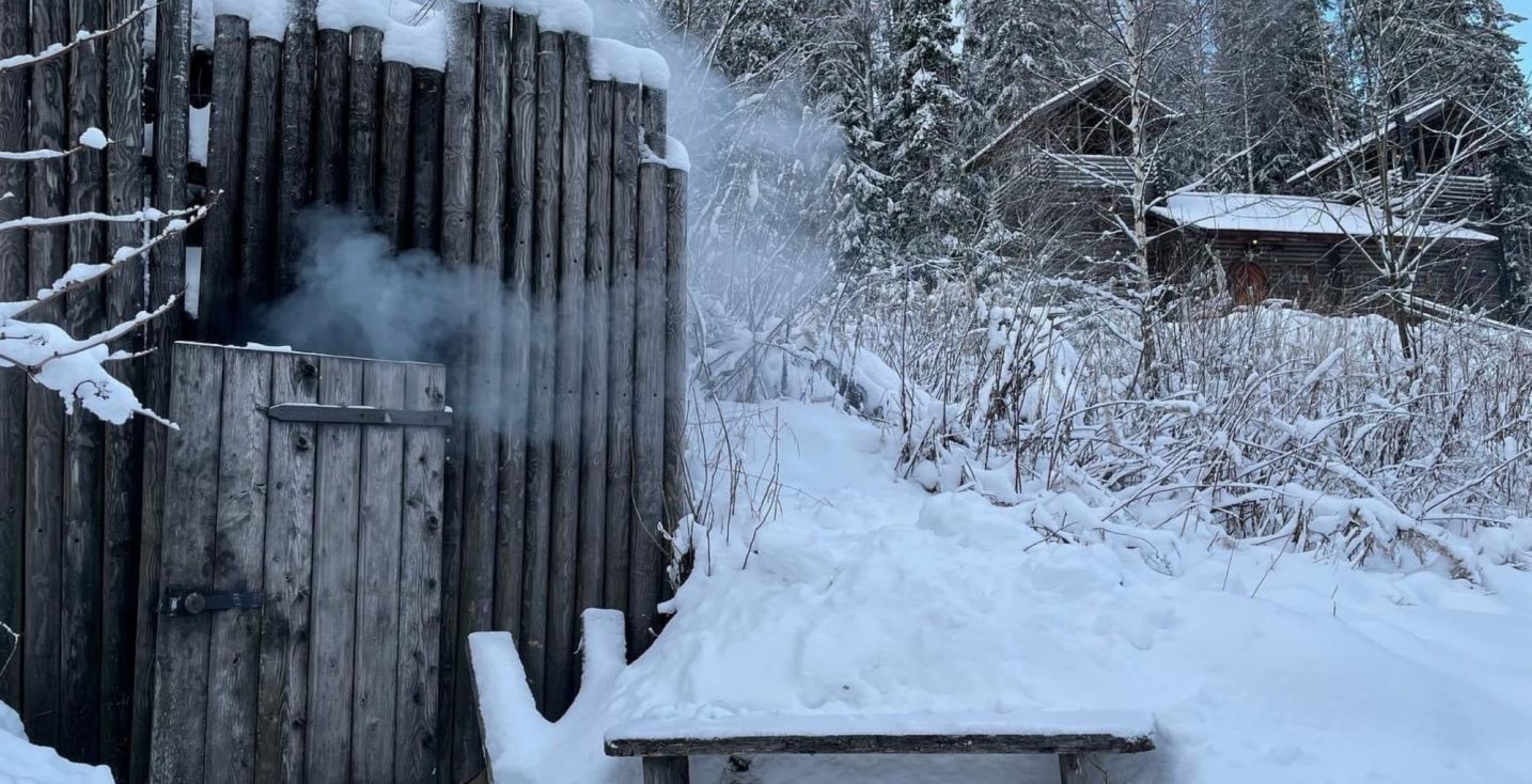 Savusaunan lämmittäminen. Härkälinnan maanalaisen savusaunan ovenraosta tupruttaa savua lumiseen aikaan, savusauna erikseen vuokrattavissa