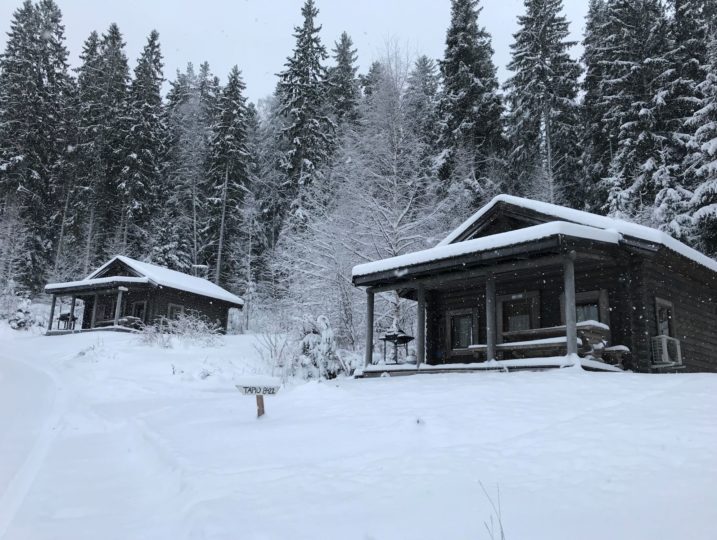 Ukko ja Tapio torpat mäenrinteessä lumihiutaleiden leijuessa talviaikaan.