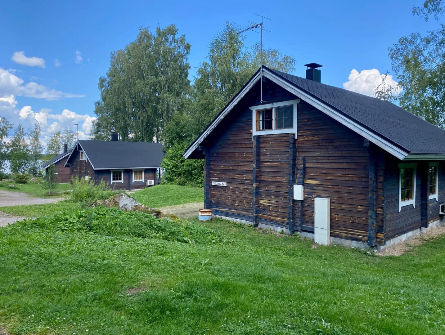 Puolukka mökki kesäisessä maisemassa, taustalla Lakka ja Varpu mökit sekä Iso-Roine.
