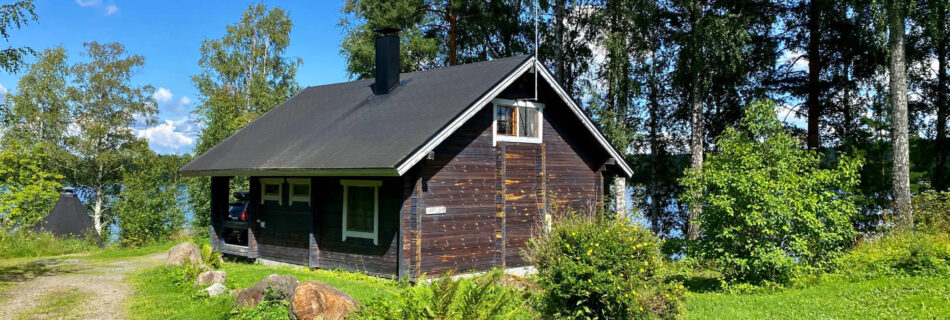 Varpu-mökki koivujen katveessa tyynellä säällä.